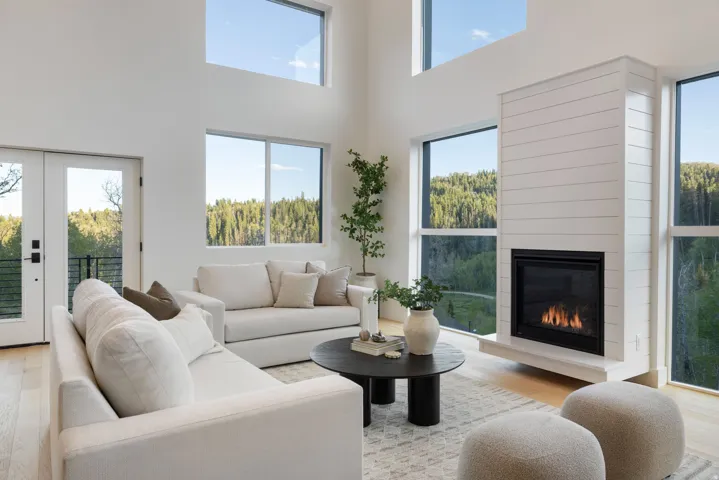 Great room featuring high ceilings, a shiplap-clad fireplace, extensive windows, light wood-finish flooring, and French doors leading to an exterior balcony