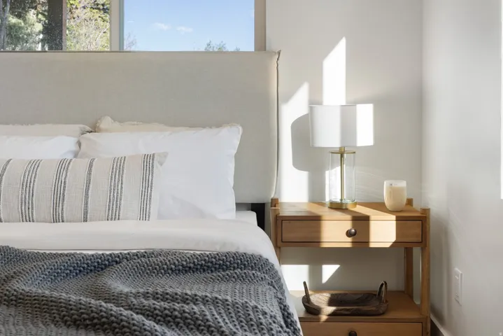 Upholstered headboard, wood-finish nightstand with integrated drawer, and a clear glass table lamp