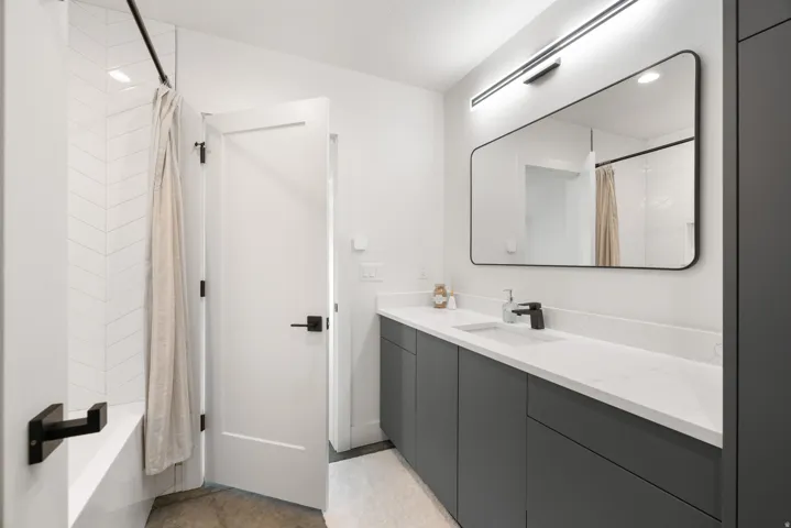 Modern bathroom featuring a long single vanity with a white countertop, dark gray cabinetry, matte black fixtures, and a rectangular mirror with backlighting