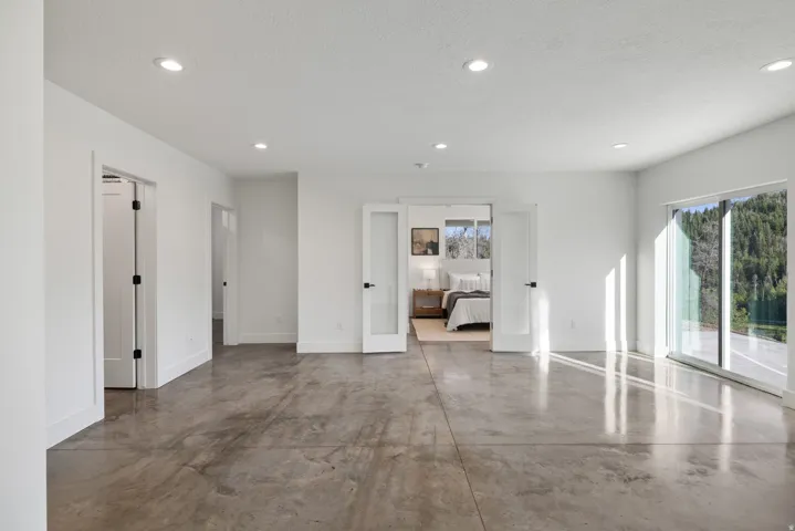 Polished concrete flooring, recessed lighting, white walls, double French doors with frosted glass, and a large sliding glass door