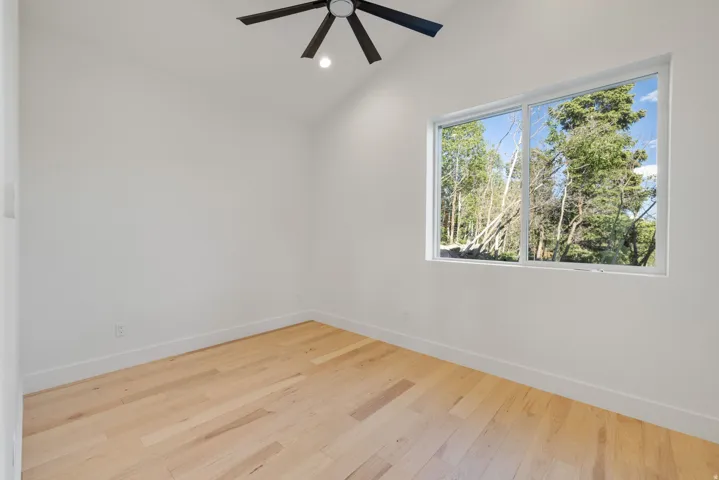 Vaulted ceiling with a black ceiling fan, wood-finish flooring, and a large window