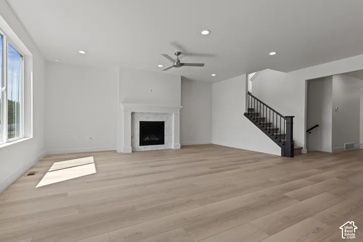 Spacious room featuring wood-finish flooring, a white mantel fireplace with a tile surround, and a ceiling fan