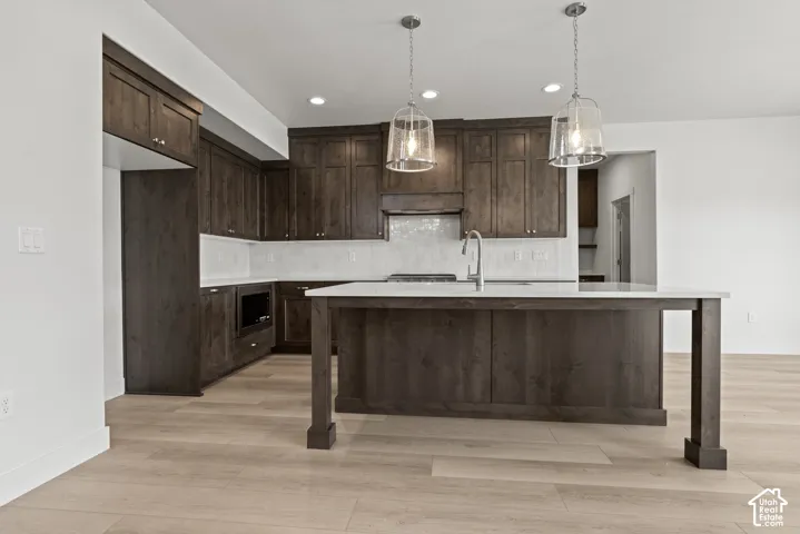 Kitchen featuring dark wood cabinetry, white countertops, a tile backsplash, and light wood-finish flooring