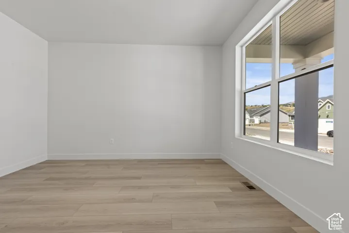 Spacious room featuring light wood-finish flooring, a large multi-pane window, bright white walls, and substantial white baseboards