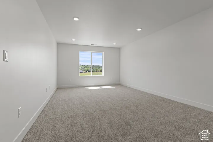 Spacious room featuring neutral carpeting, recessed ceiling lighting, a large window, white baseboards, and light-toned walls