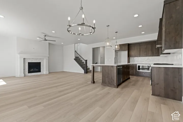 Open-concept living space featuring light wood-finish flooring throughout, a modern gas fireplace with a white mantel and tile surround, and a kitchen with dark wood cabinetry and white countertops