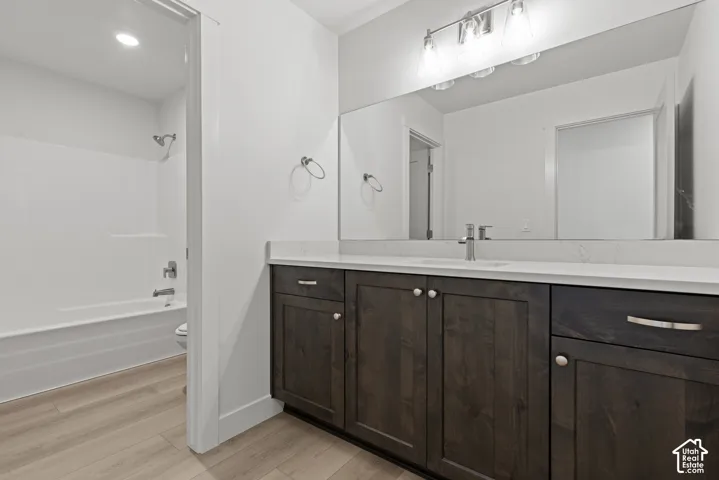 Bathroom featuring wood-finish vanity cabinetry with brushed nickel hardware, a white countertop, a wide mirror, and a white tub-shower combination