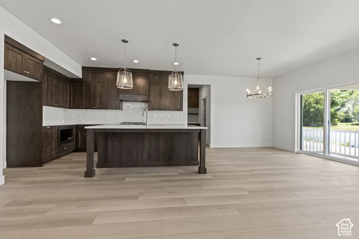 Spacious kitchen and living area featuring wood-finish flooring, dark wood cabinetry, and a kitchen island with a light-colored countertop