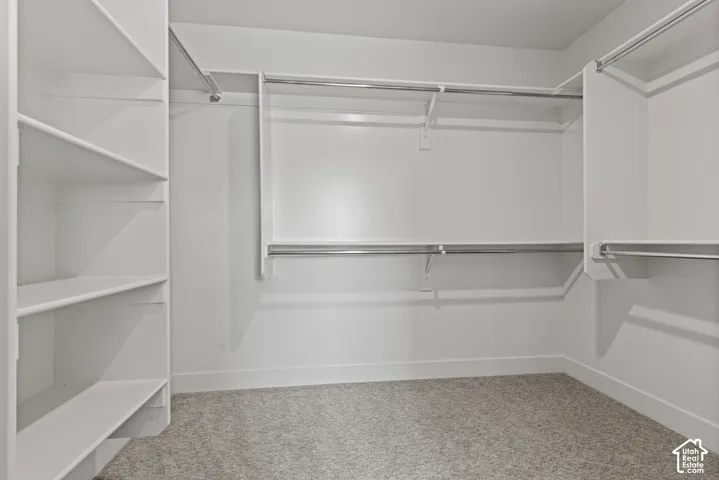 Spacious walk-in closet featuring white built-in shelving, chrome hanging rods, white walls, and a light-toned carpet