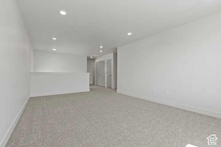 Spacious carpeted room featuring recessed lighting, light gray wall-to-wall carpeting, white baseboards, and a white interior railing