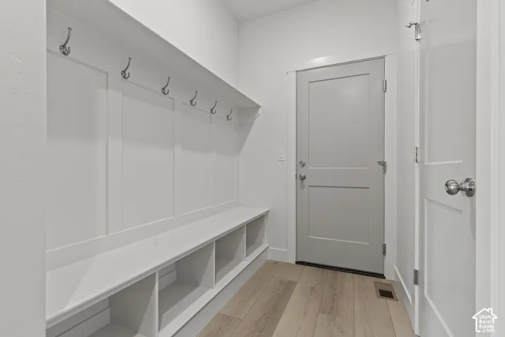 Entryway featuring light wood-finish flooring, white built-in storage bench with cubbies, white wainscoting with coat hooks, and a gray panel door with brushed nickel hardware