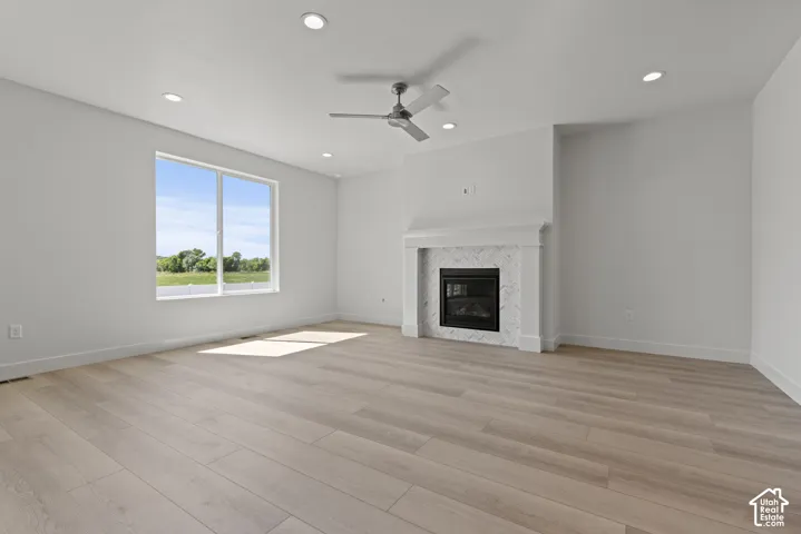 Spacious room featuring light wood-finish flooring, a contemporary fireplace with a decorative tile surround and mantel, a ceiling fan, recessed lighting, and a large window providing ample natural light and a green landscape backdrop