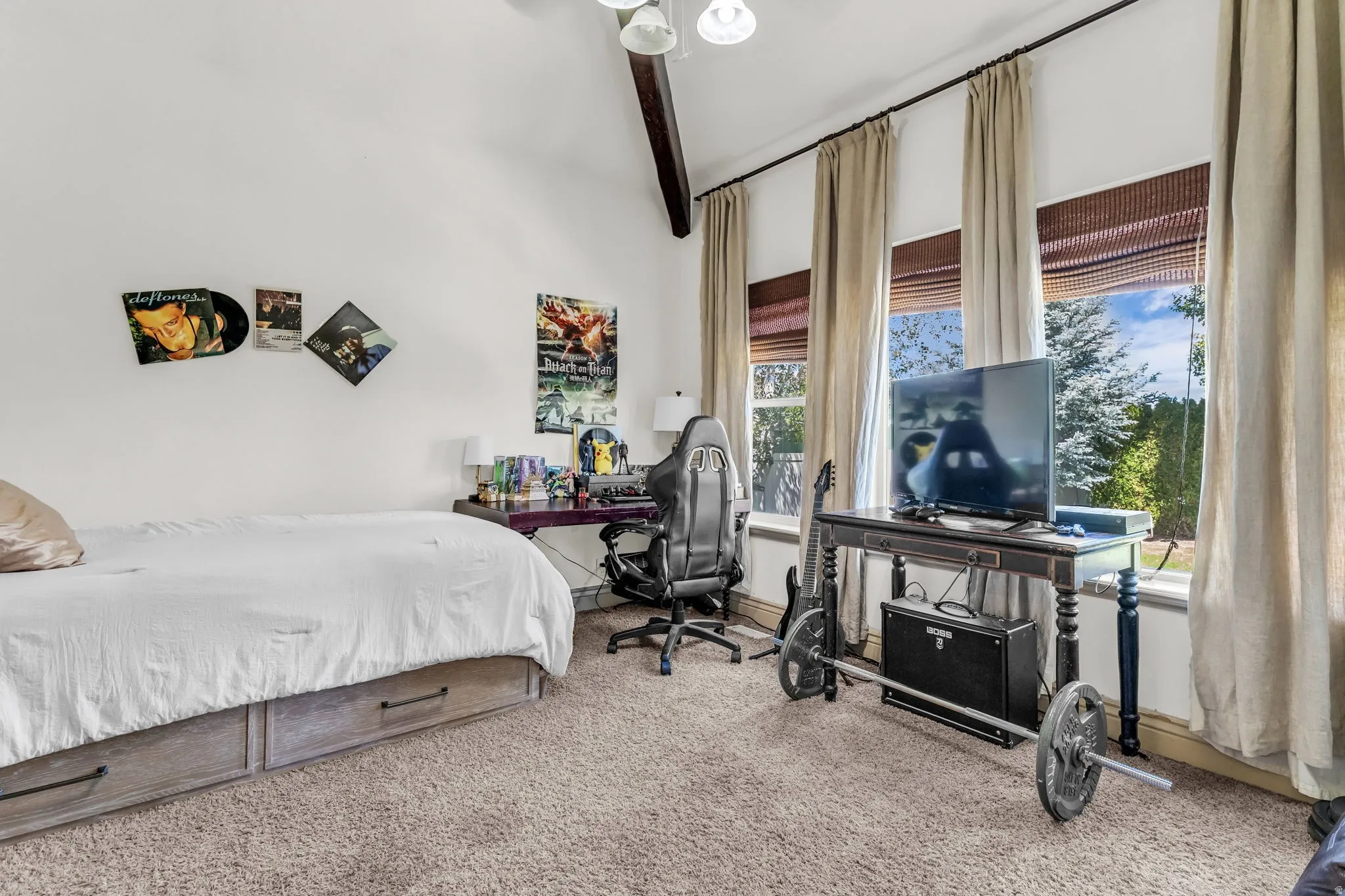Main level master suite with a  vaulted ceiling with exposed wood beam, three large windows with blinds and drapes