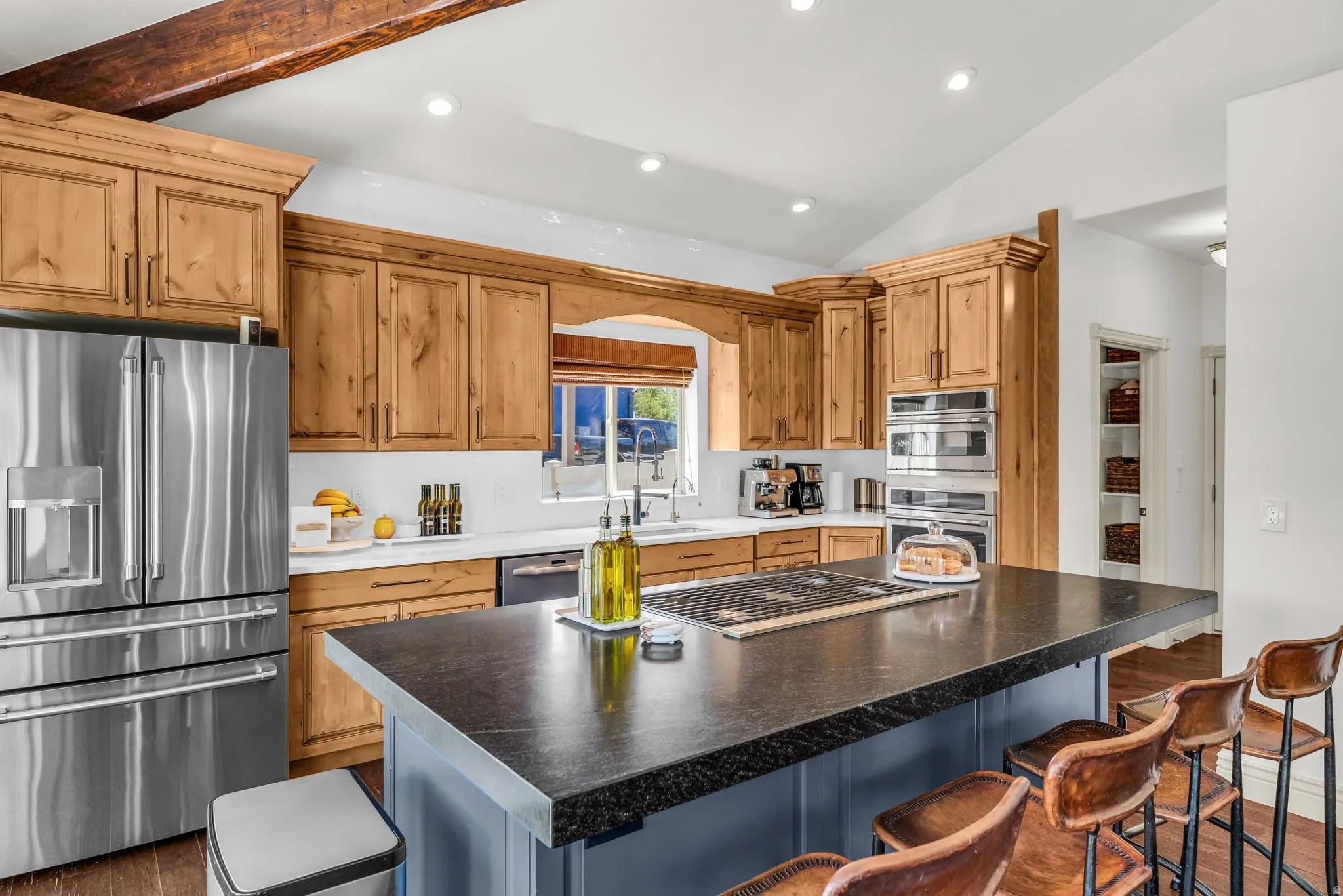 Kitchen featuring knotty alder cabinetry, stainless steel appliances, a center island with a dark countertop, and exposed wood ceiling beams