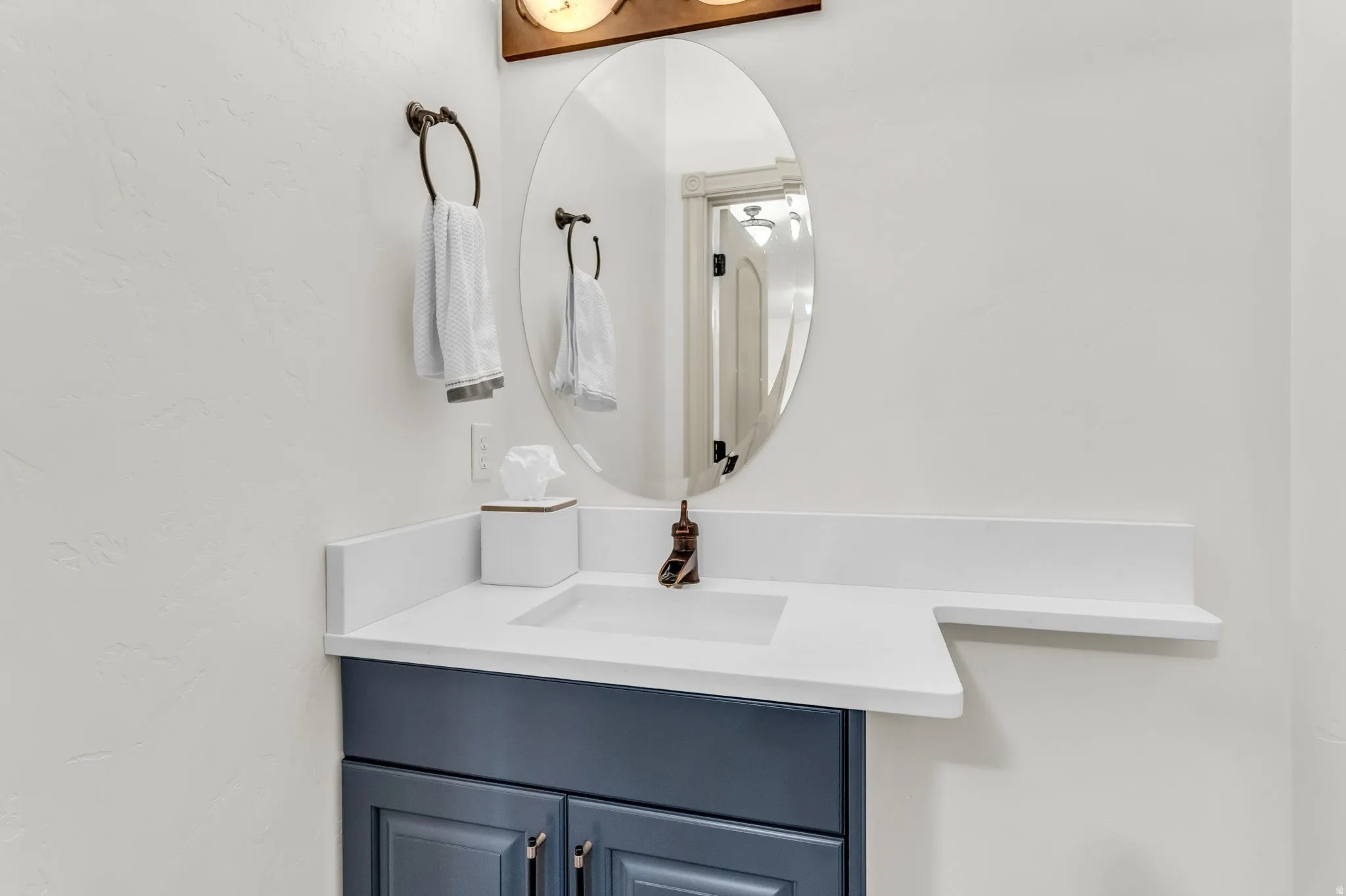 Newly renovated Half Bathroom in main level features an oval mirror over a white countertop with an integrated sink and bronze-finish faucet
