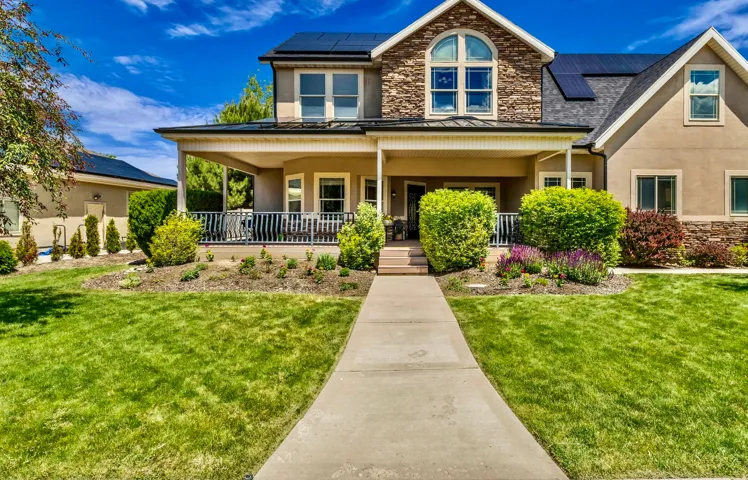 Two-story residence featuring stone and stucco exterior finishes, a covered front porch, and solar panels