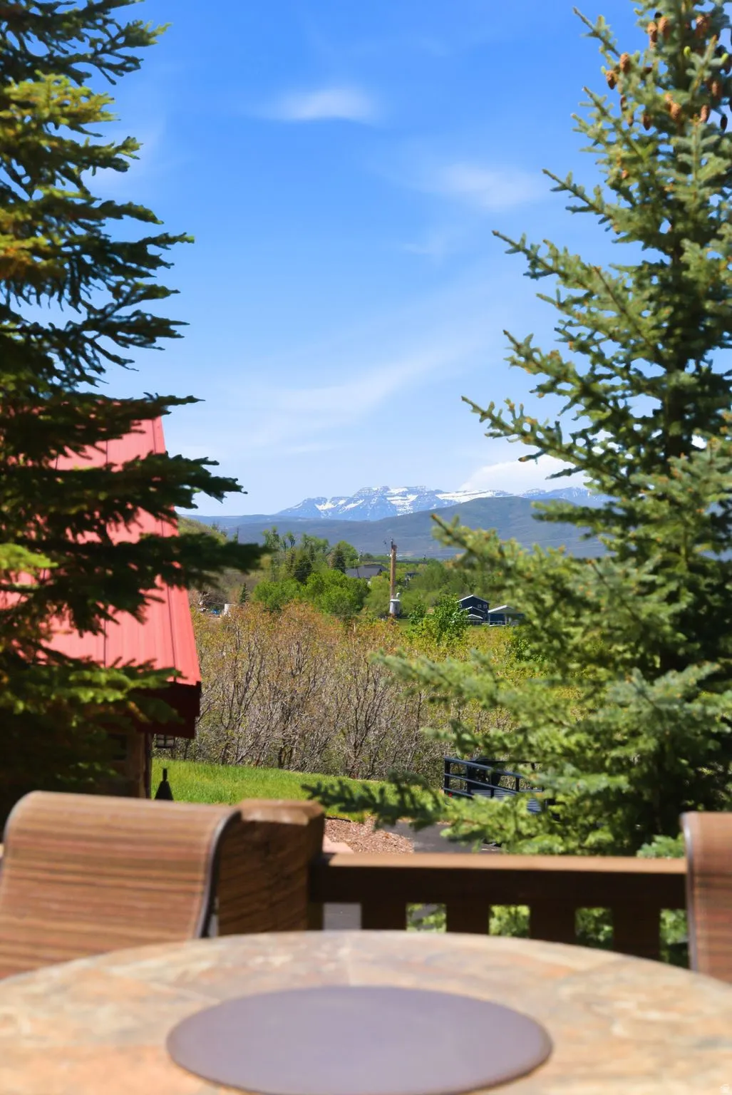 Outdoor deck area with a stone-finish table, offering distant mountain scenery and mature evergreen trees