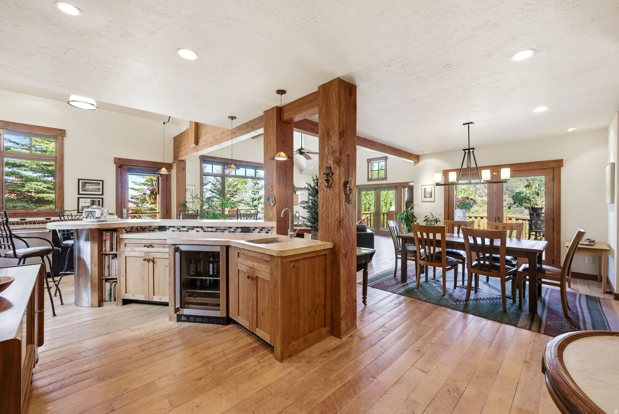 Open-concept living area featuring blonde wood-finish flooring, exposed wood beams, and recessed lighting