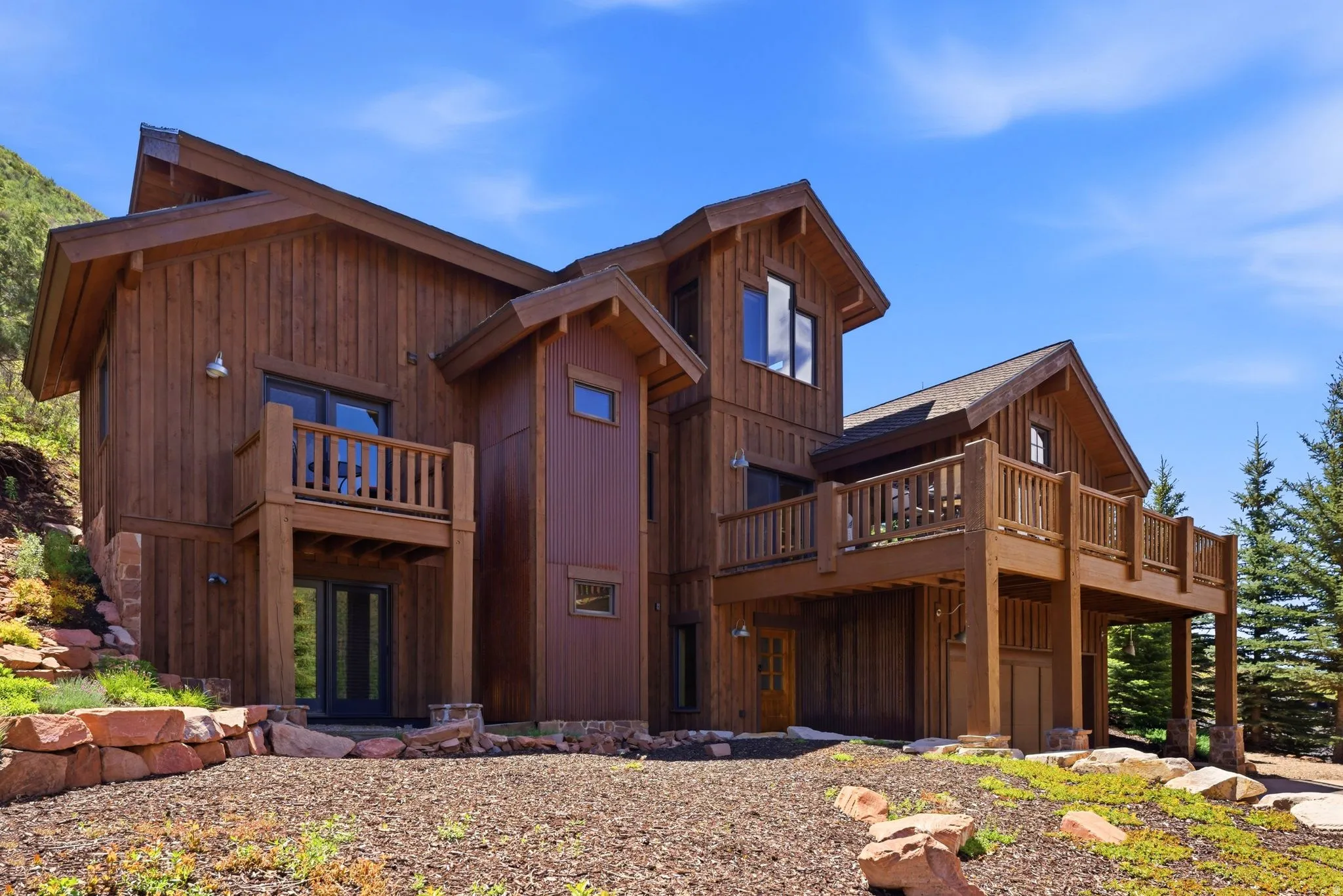 Multi-level residential exterior featuring warm wood siding, a prominent gabled roofline, and multiple outdoor deck spaces