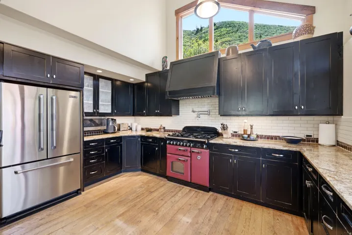Kitchen featuring AGA range oven, stainless steel refrigerator, black cabinetry, light-toned countertops, and wood-finish flooring