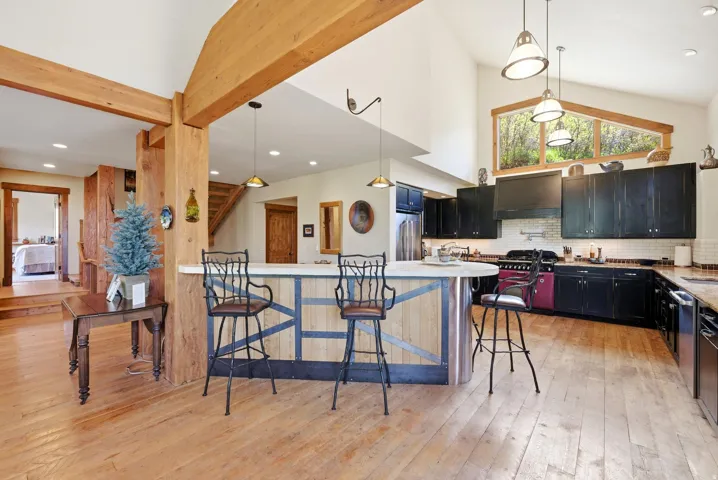 Open-concept kitchen featuring wood-finish flooring, vaulted ceilings, exposed timber beams, black cabinetry, and a AGA range and ovens.