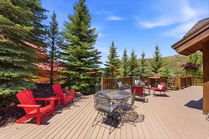 Expansive outdoor deck featuring wood-finish flooring, a wood-railed perimeter, and mature evergreen trees