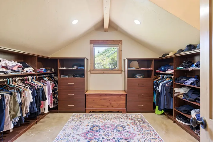 Attic conversion featuring vaulted ceilings with exposed beam, recessed lighting, wood-framed window, and built-in wood-finish closet organizational systems