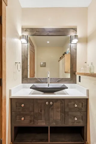 Wood-finish vanity with a white countertop and a dark vessel sink