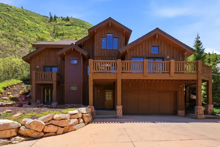 Multi-level wood-clad exterior featuring multiple balconies, a lower-level garage, and a stacked stone retaining wall