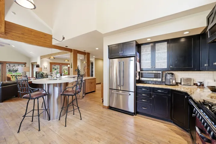 Expansive kitchen featuring wood-finish flooring, stainless steel appliances, dark cabinetry, and granite countertops