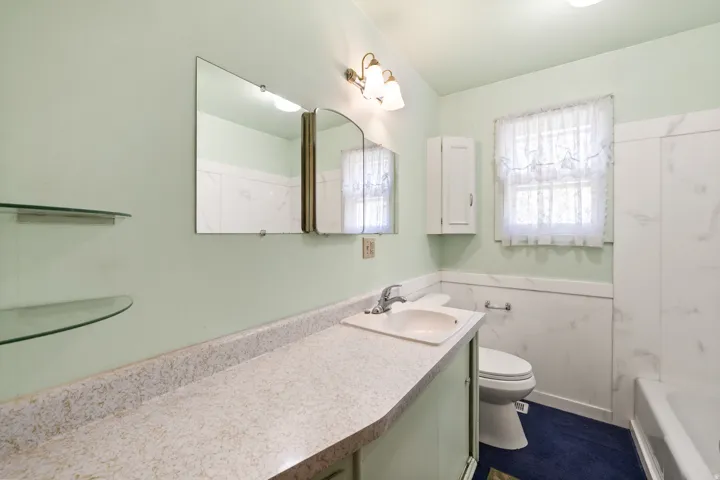 Bathroom featuring a vanity with an integrated sink, a wall-mounted mirror, and glass shelving