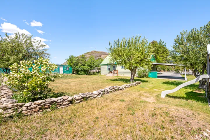 Spacious outdoor area featuring a dry-stacked stone retaining wall, mature trees, and a detached carport