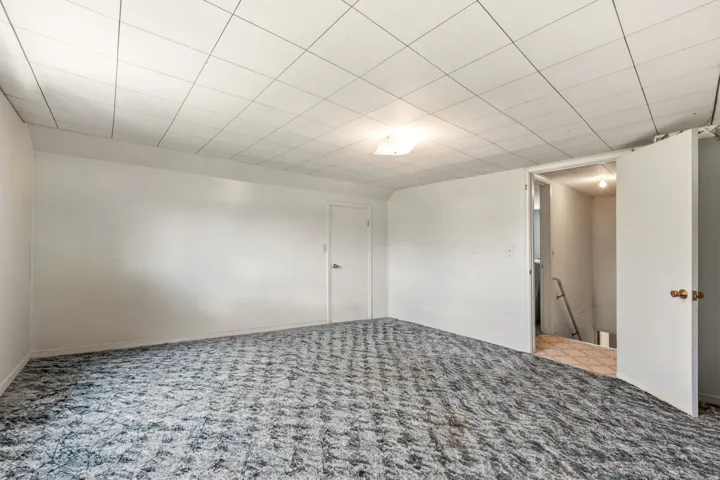 Spacious room featuring textured carpeting, white painted walls, and a dropped ceiling with recessed lighting