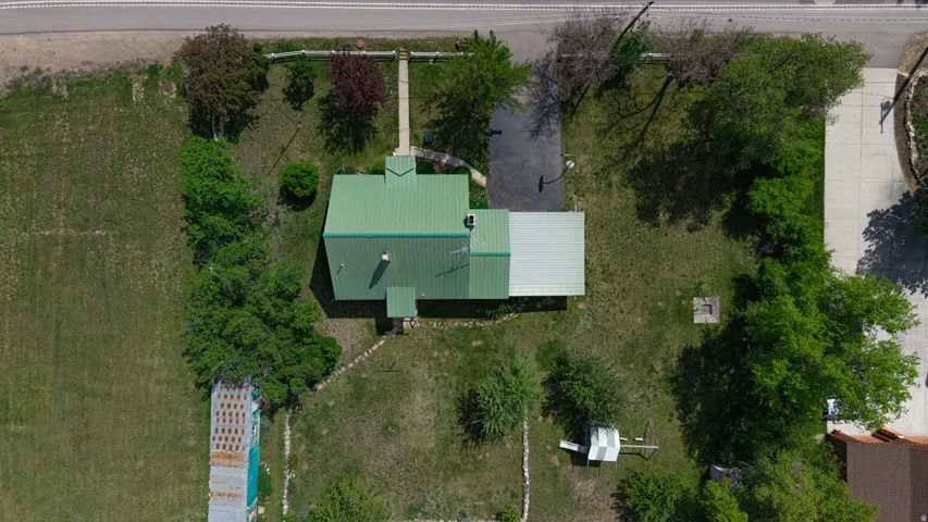 Property featuring a green metal roof, expansive green space, mature trees, and a concrete driveway