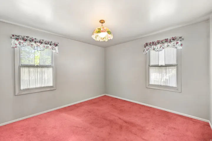 Bright room featuring twin windows, light-colored walls, red carpeting, white trim, and an overhead light fixture