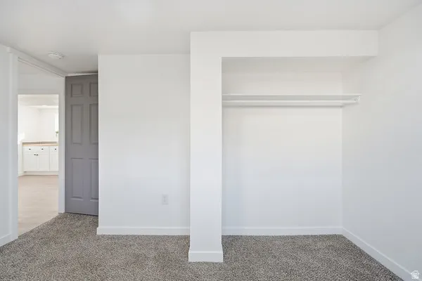 Room featuring light gray carpeting, crisp white walls, and an open closet with a hanging rod