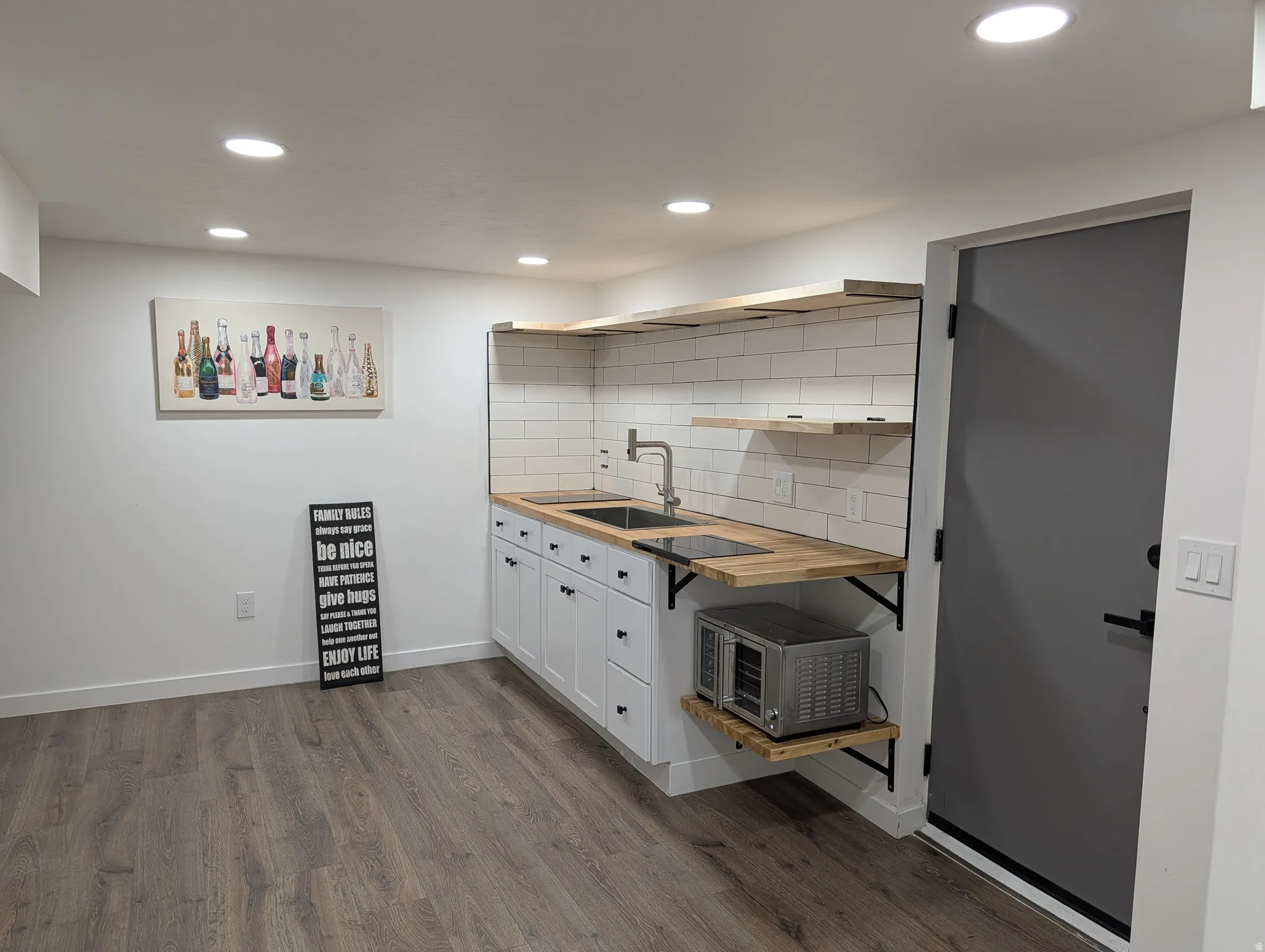 Wet bar featuring dual sinks, wood-finish countertops, and a subway tile backsplash
