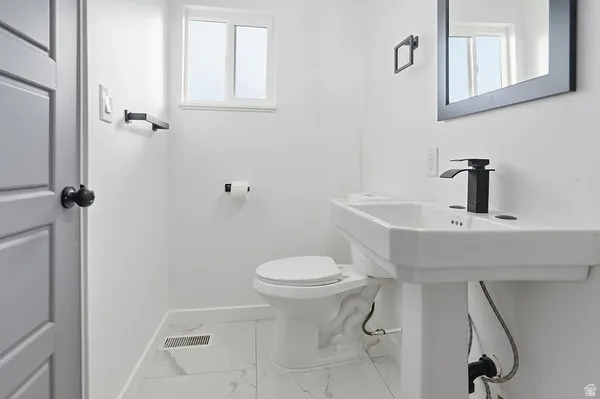 Modern bathroom featuring a pedestal sink with a matte black faucet, framed mirror, and white square tile flooring