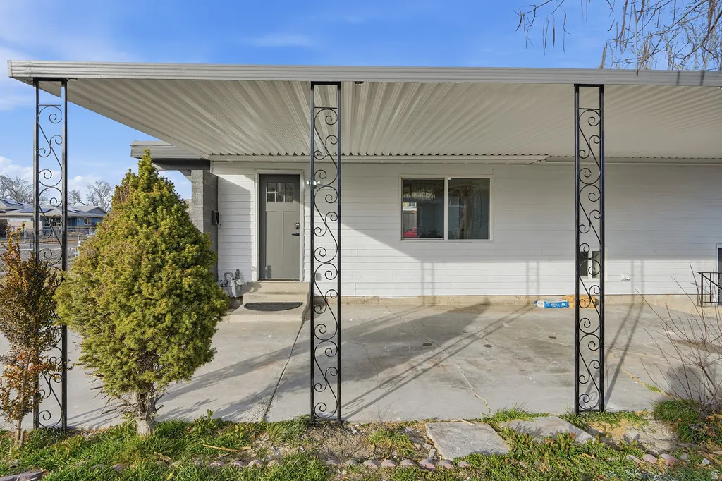 Covered concrete patio featuring decorative wrought iron columns, white siding, and a paneled entry door with frosted glass