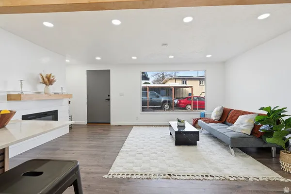 Open-concept living area featuring recessed lighting, wood-finish flooring, a contemporary fireplace with a white shiplap surround, and a large window