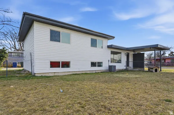 Rear exterior featuring white horizontal siding, a covered patio area with a dark gray flat roof, and an air conditioning unit