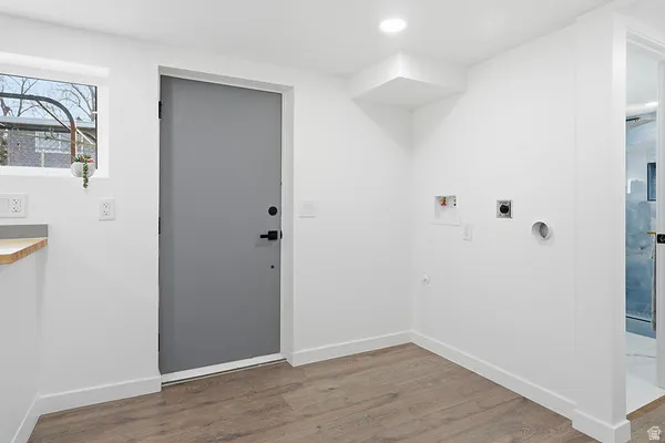 Dedicated laundry area featuring wood-finish flooring, a contemporary gray door with black hardware, and an overhead recessed light
