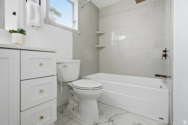 Bathroom featuring a white vanity with gold-toned hardware, a white toilet, and a bathtub with subway tile surround