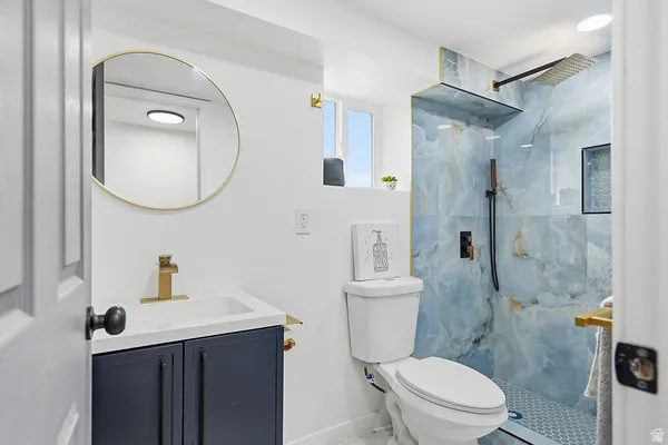 Contemporary bathroom featuring a vanity with a white countertop and blue cabinetry, a round gold-framed mirror, and a walk-in shower with blue-toned tile, a rain showerhead, and a recessed niche
