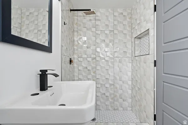Bathroom featuring a rectangular sink with matte black faucet, framed mirror, and walk-in shower with textured tile surround, a built-in niche, and hexagonal floor tile