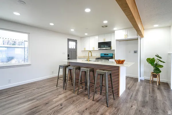 Contemporary kitchen featuring white cabinetry with gold-tone hardware, a center island with slatted wood-finish paneling and a light-toned countertop, and recessed lighting throughout