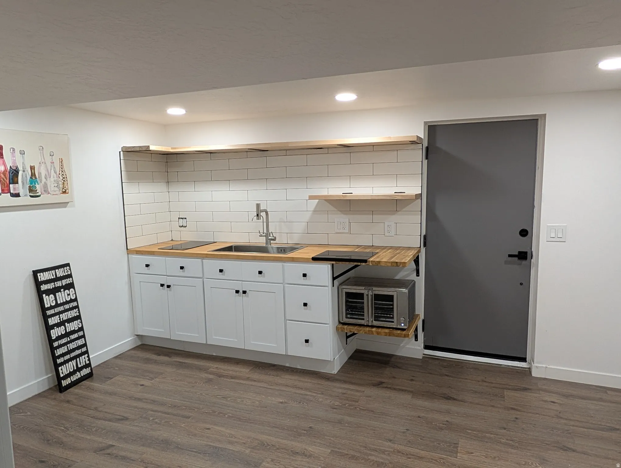 Compact kitchen area featuring white shaker-style cabinetry, wood-finish countertops, and a subway tile backsplash