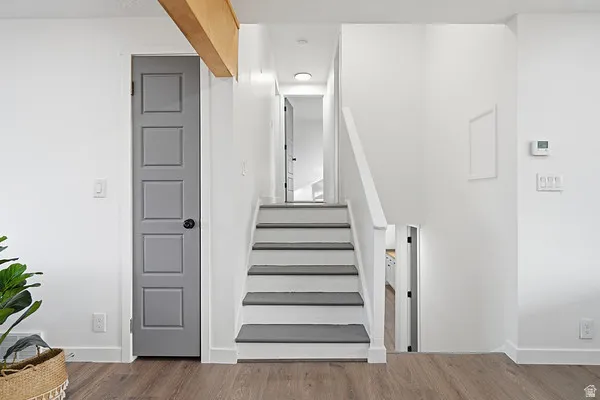 White painted staircase featuring dark treads and risers, wood-finish flooring, and a contemporary gray paneled door with black hardware