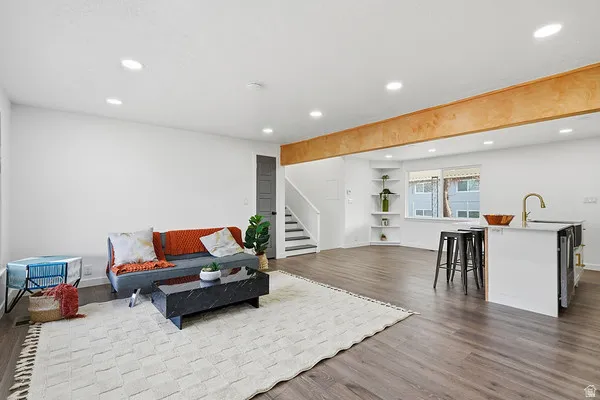 Expansive open-concept living area featuring wood-finish flooring, recessed lighting, and a prominent wood-toned ceiling beam