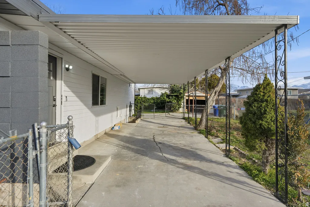 Covered side patio featuring an extended roofline with decorative wrought iron supports and concrete surfacing